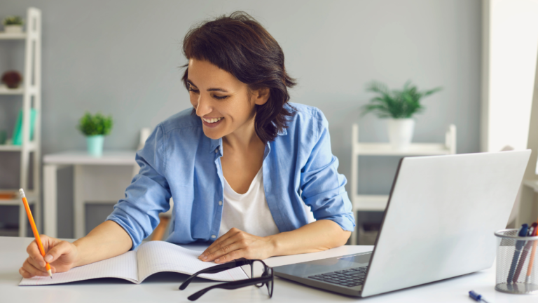 A woman who is taking notes sitting in front of a laptop