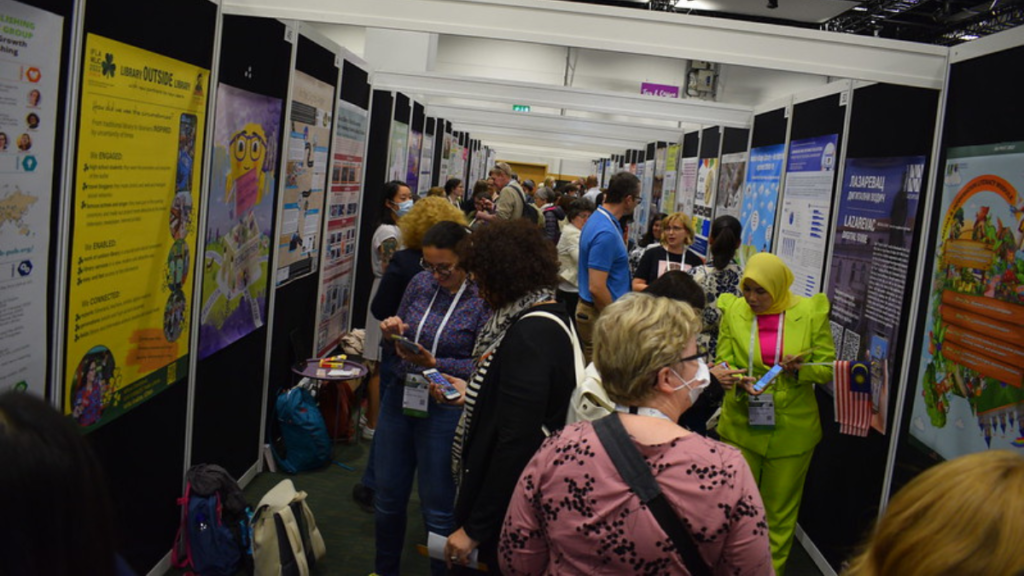 An image of people walking and standing by posters during a WLIC poster session