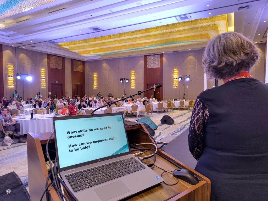 An image of a person standing in a room next to a laptop with text